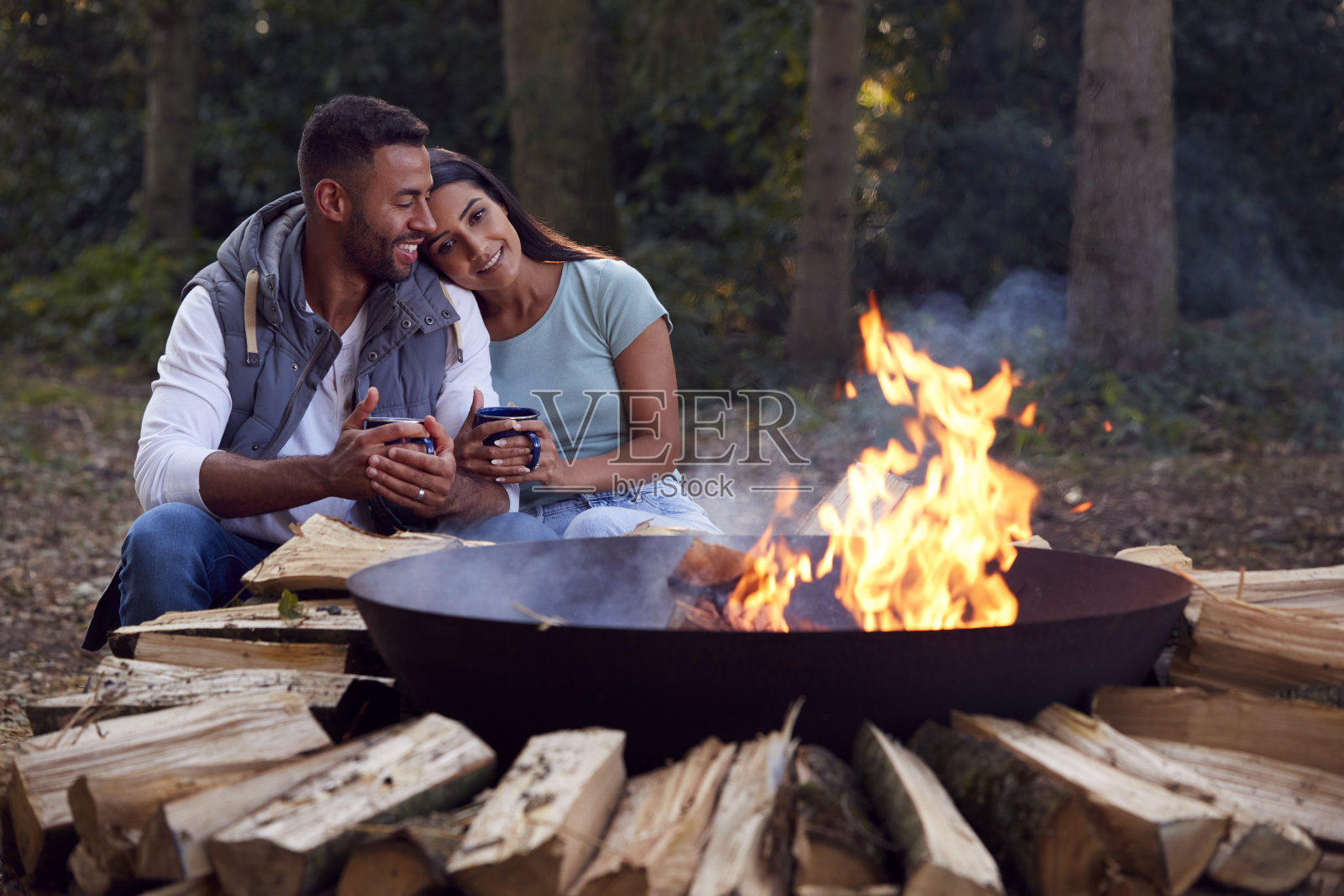 浪漫的情侣露营坐在篝火旁的火碗和热饮照片摄影图片
