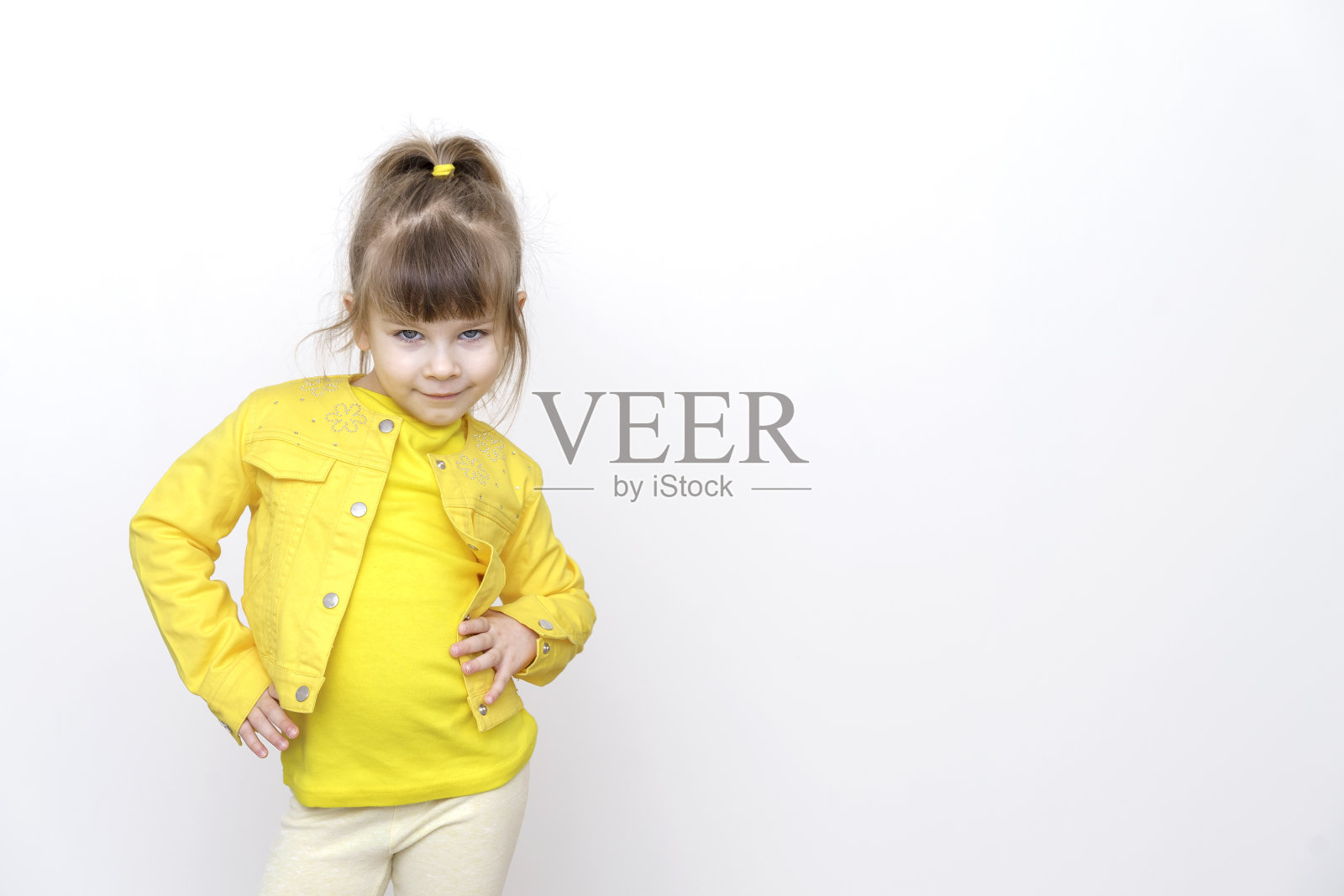 穿着黄色衣服的小女孩在灰色墙壁的背景下摆姿势照片摄影图片
