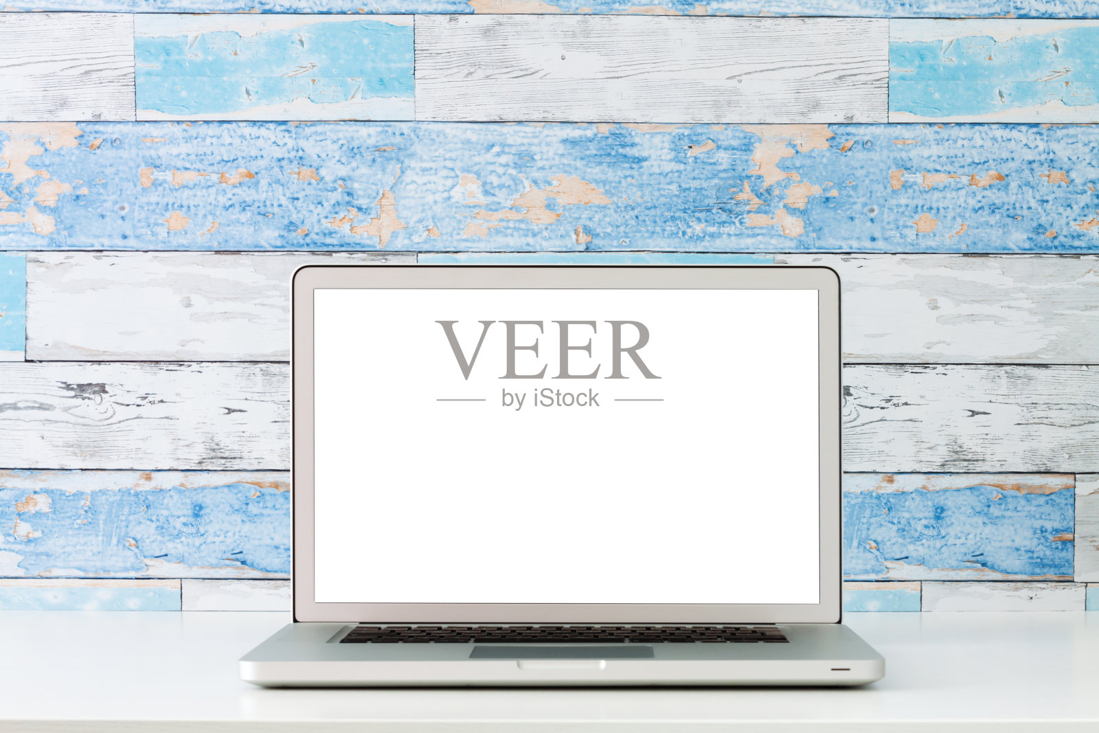 一个打开的笔记本电脑在一张白色的桌子上。模型。用旧的蓝色木板砌成的墙。照片摄影图片