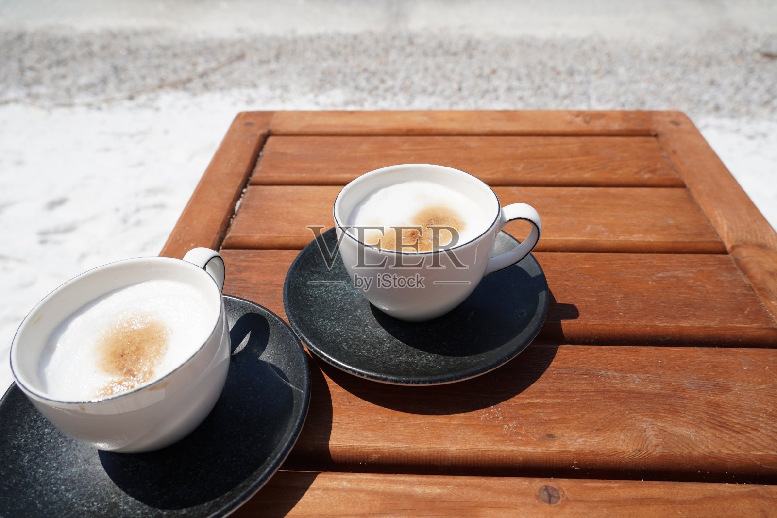 白色的咖啡卡布奇诺和灰色的茶托放在海滩的木桌上，翠绿色的海洋，白色的船在背景，美妙的看风景照片摄影图片