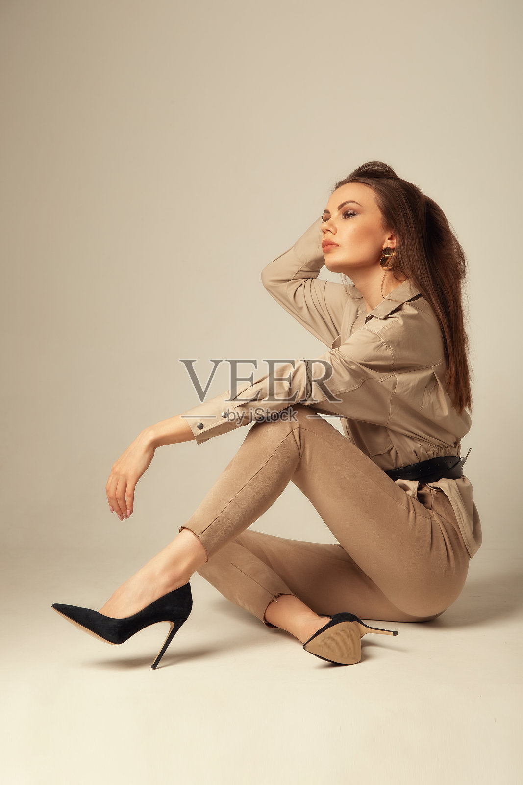 一名年轻的白人女子在米色衬衫摆姿势在地板上，看着米色背景的相机的肖像照片摄影图片