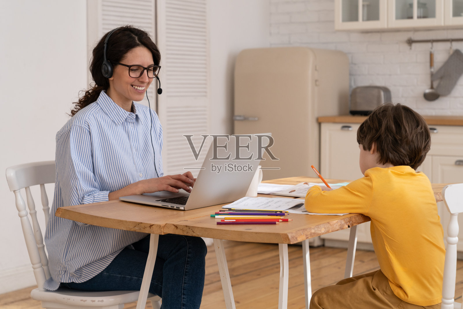 妈妈和小儿子在厨房远程工作。年轻的女商人在家办公室和小男孩画照片摄影图片