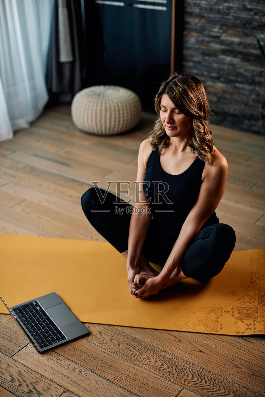 平静的中年瑜伽教练坐在家里，用笔记本电脑在线授课。照片摄影图片