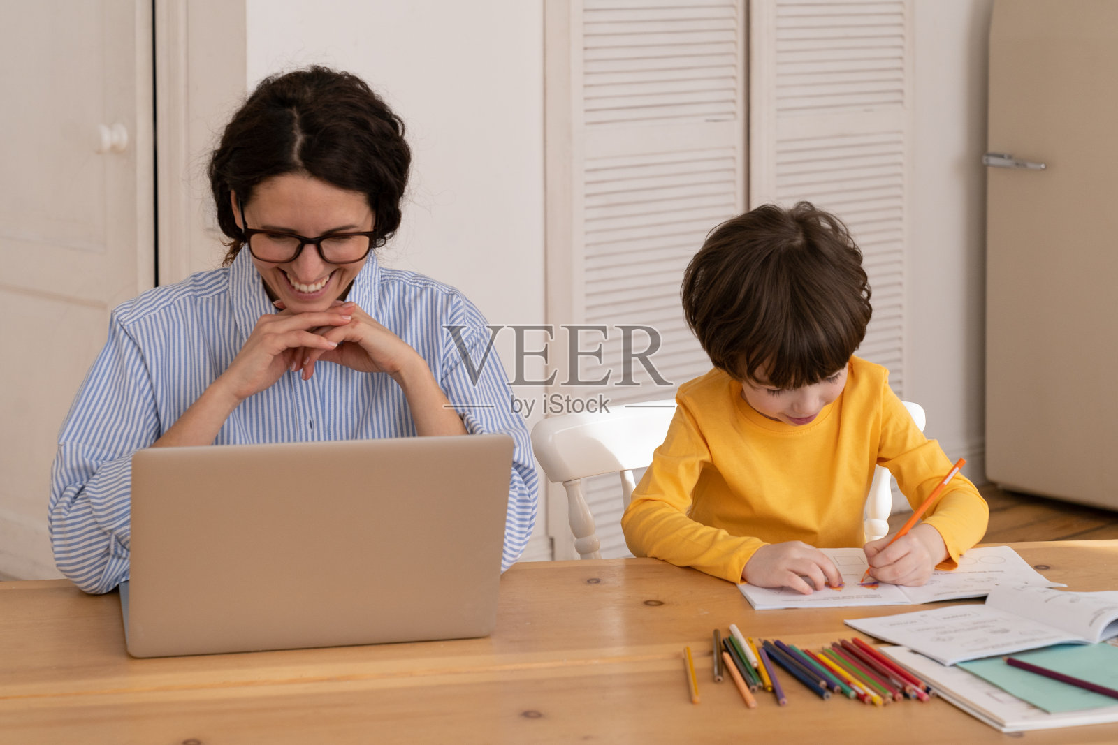 新冠肺炎一级防范禁闭期间，千禧一代商界女性在家用笔记本电脑工作，带着年幼的儿子坐在办公桌前照片摄影图片