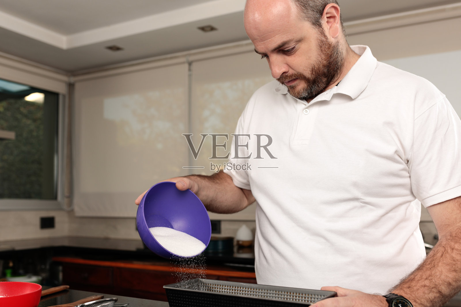 白人男性，30-39岁之间，秃顶，在碗里撒糖或面粉，准备蛋糕，在家庭厨房。照片摄影图片