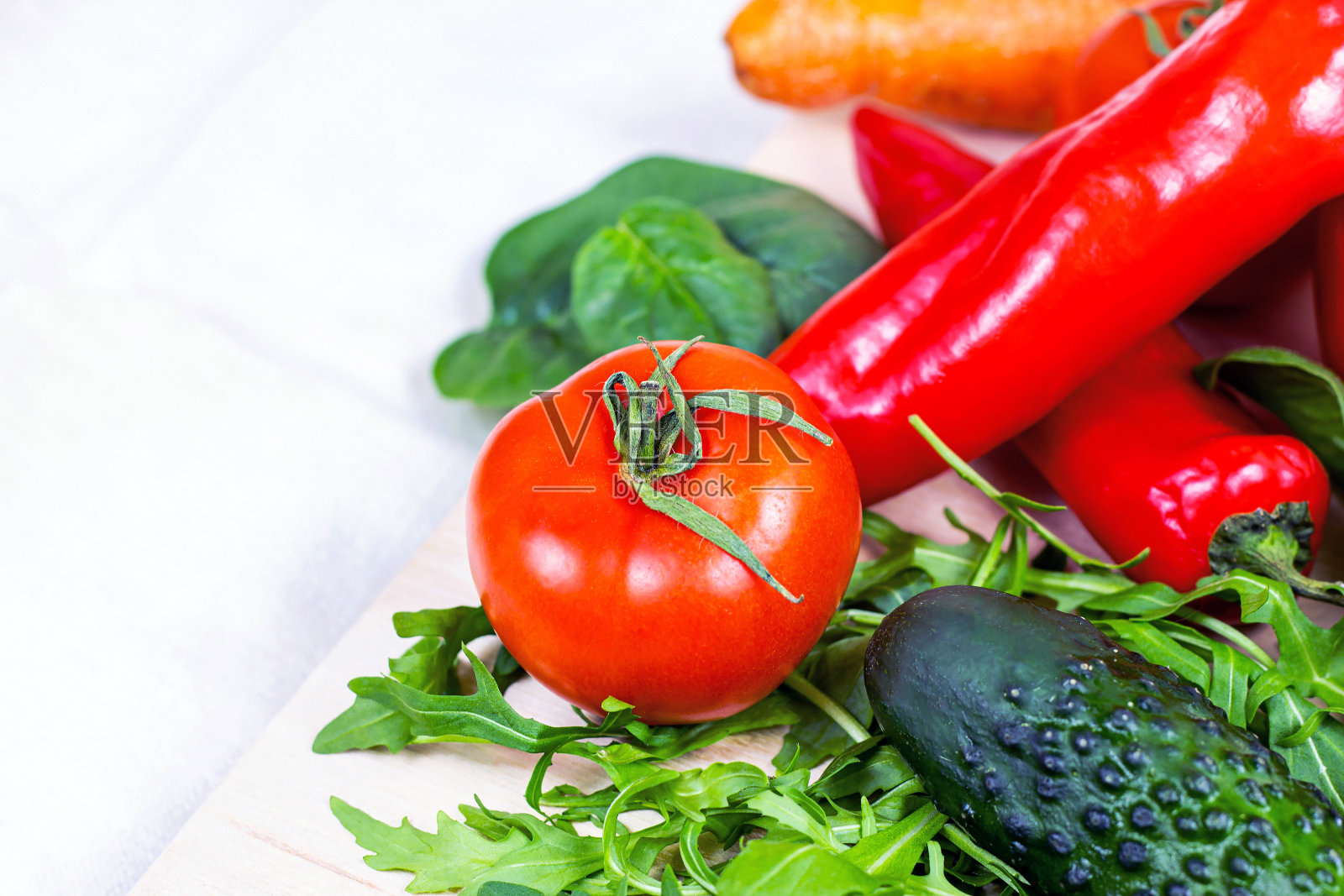 新鲜的农场夏季蔬菜沙拉:黄瓜，番茄，洋葱，芝麻菜叶在厨房的光背景照片摄影图片