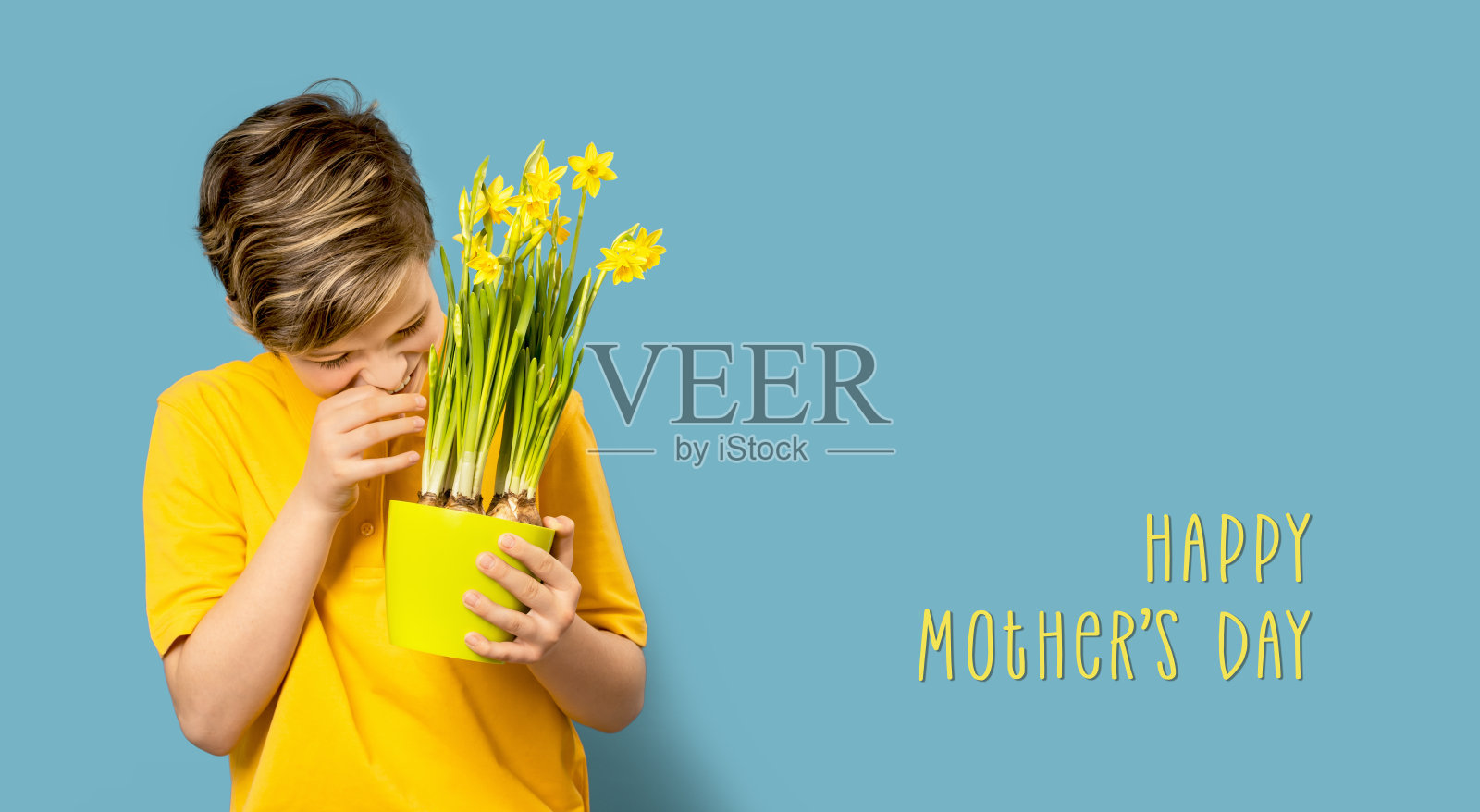 微笑的男孩躲在水仙花后面。蓝色的母亲节卡片照片摄影图片