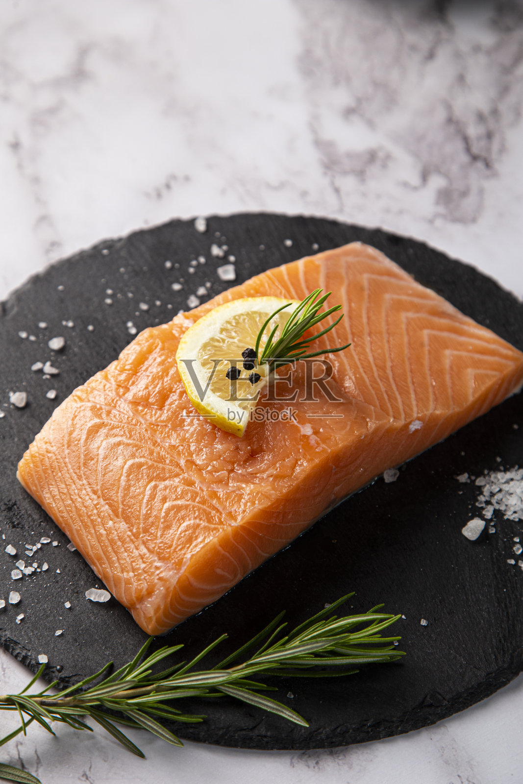 生鲑鱼装在石板盘子里，桌上有柠檬和迷迭香照片摄影图片