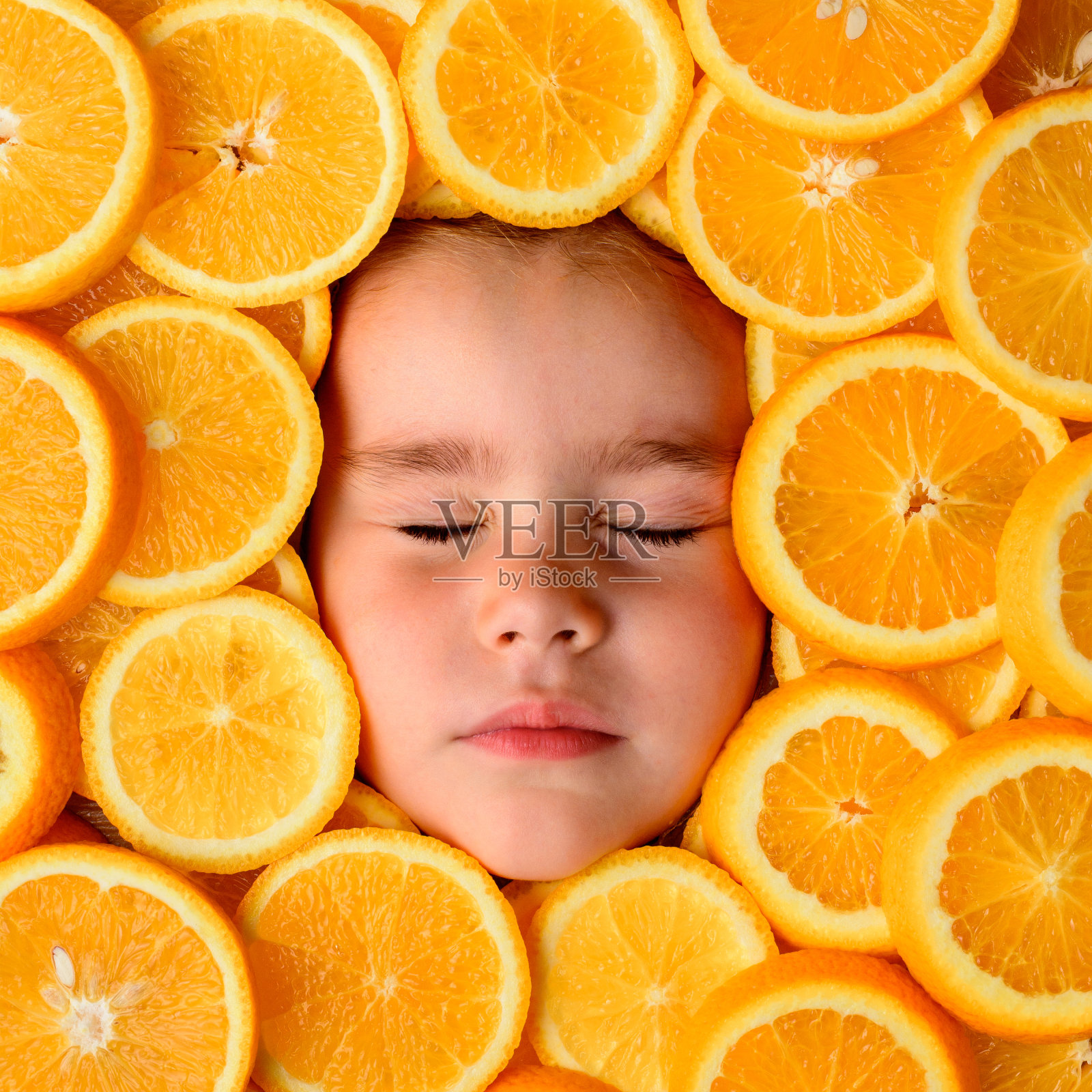 一个美丽的小女孩的脸被一块块的橙子片包围着，橙子是富含维生素C的有益水果。照片摄影图片