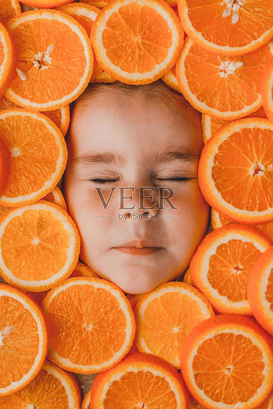 一个美丽的小女孩的脸被一块块的橙子片包围着，橙子是富含维生素C的有益水果。照片摄影图片