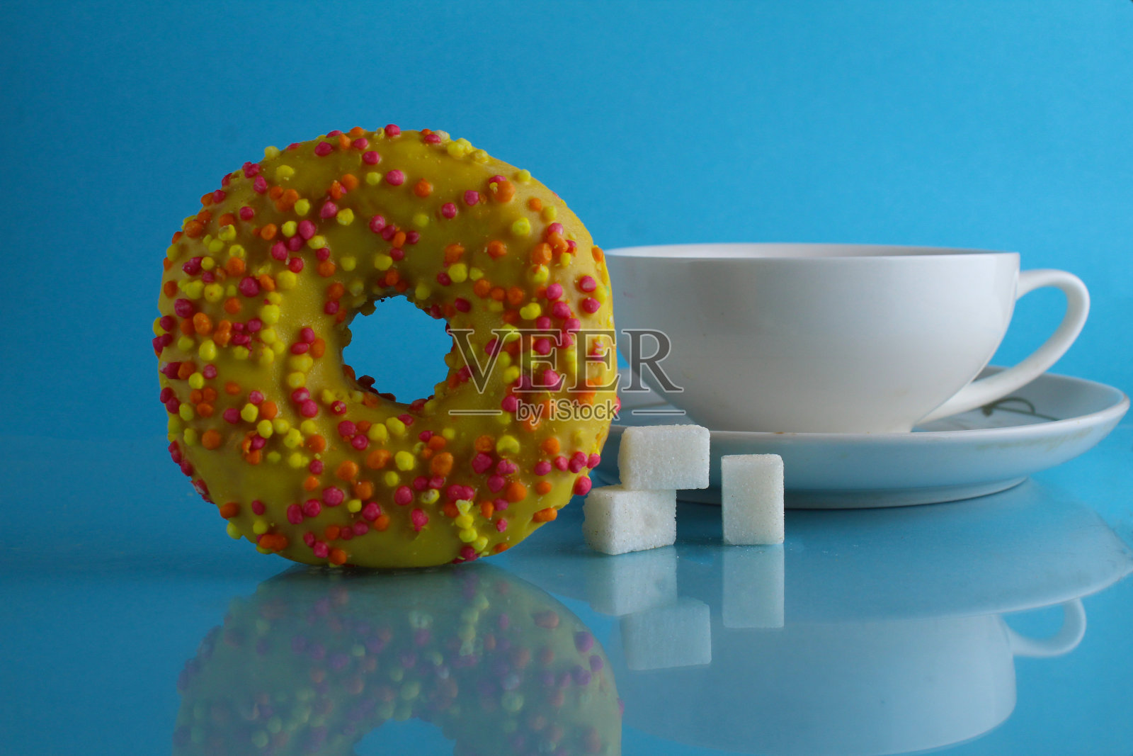 静物甜甜圈黄色粉色黄色巧克力和一杯茶咖啡在蓝色明亮的背景。一天不节食。厨房海报照片摄影图片