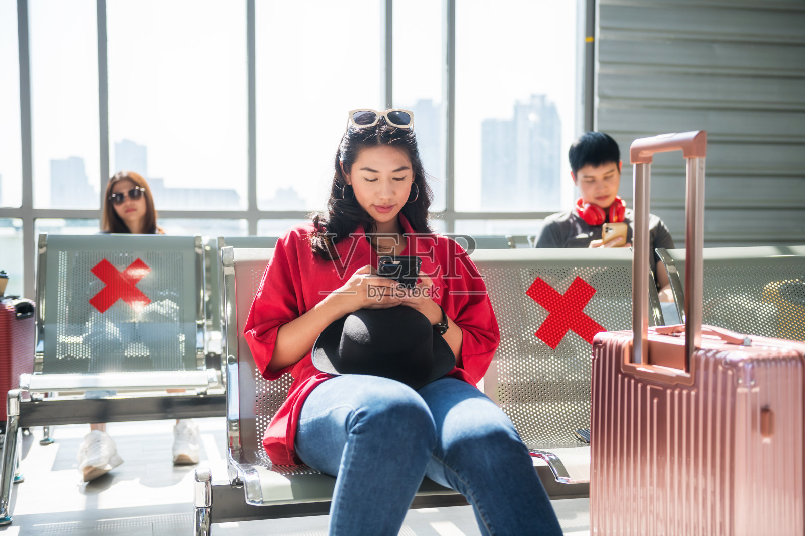 女孩在机场候机楼玩手机。社会距离照片摄影图片