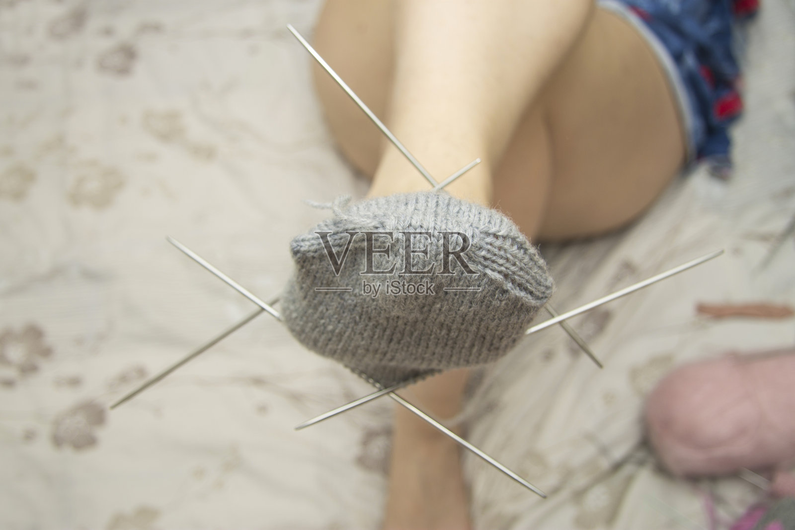 一个女人在浅色的背景上试穿一只未完成的灰色羊毛袜子照片摄影图片