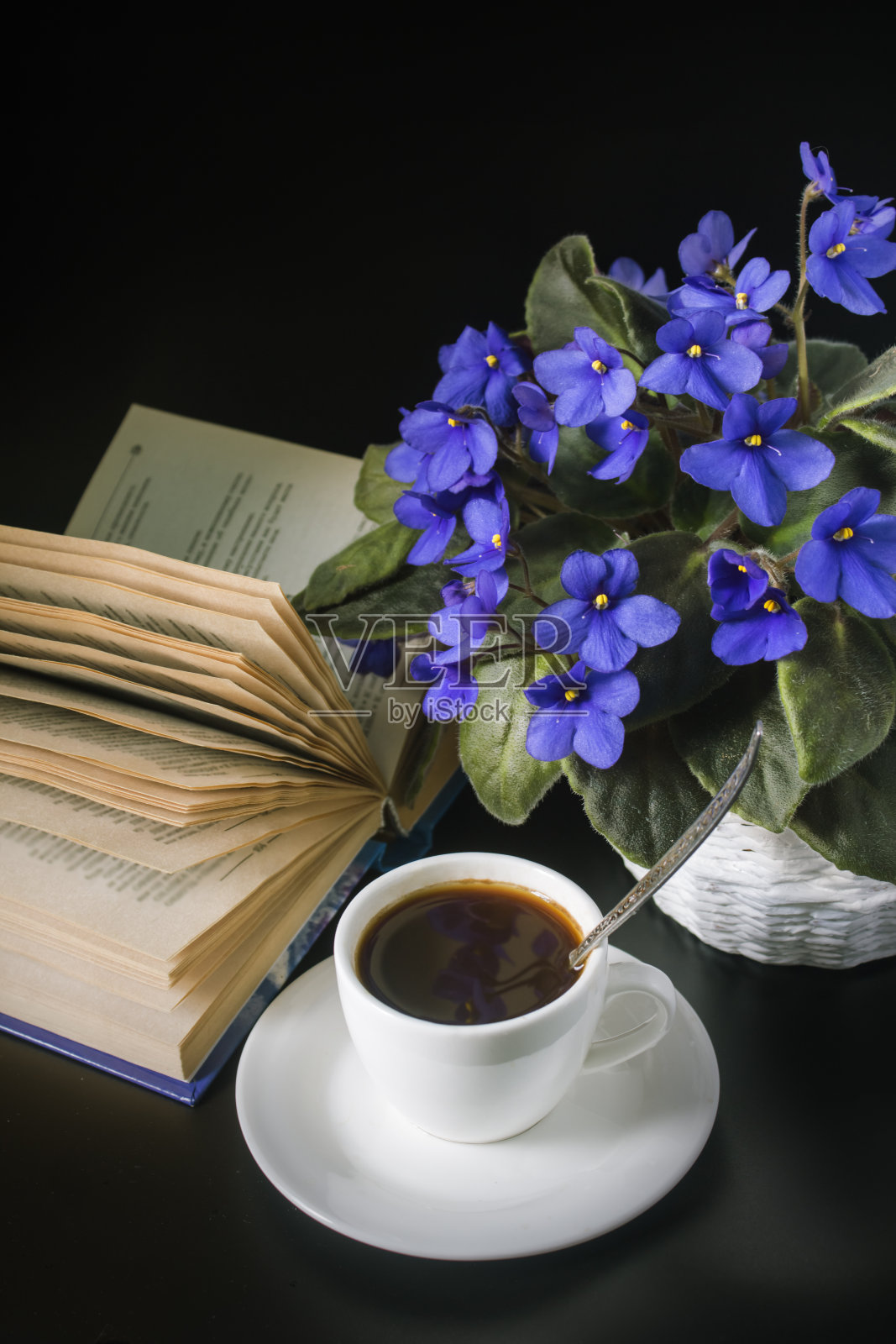 一束非洲紫罗兰，一杯咖啡，一本打开的书在黑色背景上照片摄影图片