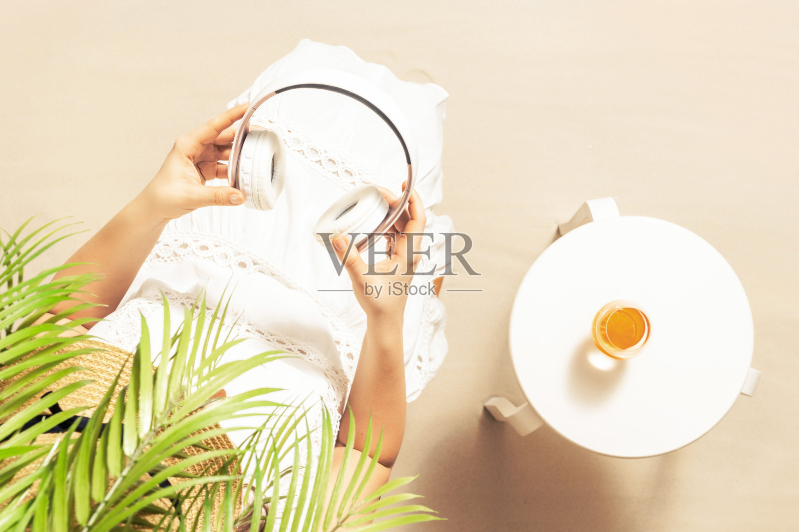 独自坐在棕榈树下的女人。桌上放着一杯橙汁和耳机。暑假女性在沙滩上放松。俯视图照片摄影图片