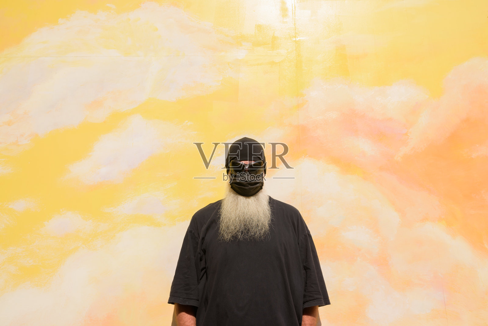 夏日的成年男子肖像，留着长长的灰胡子，戴着墨镜，背靠阴云密布的背景墙，戴着口罩，以防止Covid-19照片摄影图片