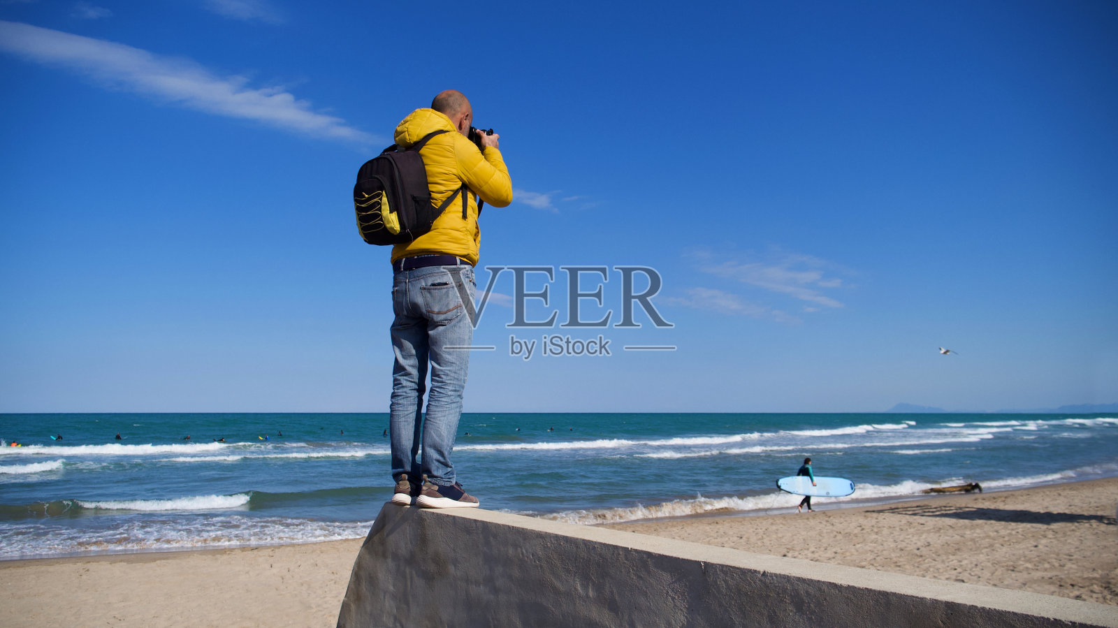 一个不知名的男人和他的摄影器材在一个阳光明媚的日子与蓝色的天空在海滩上拍照照片摄影图片