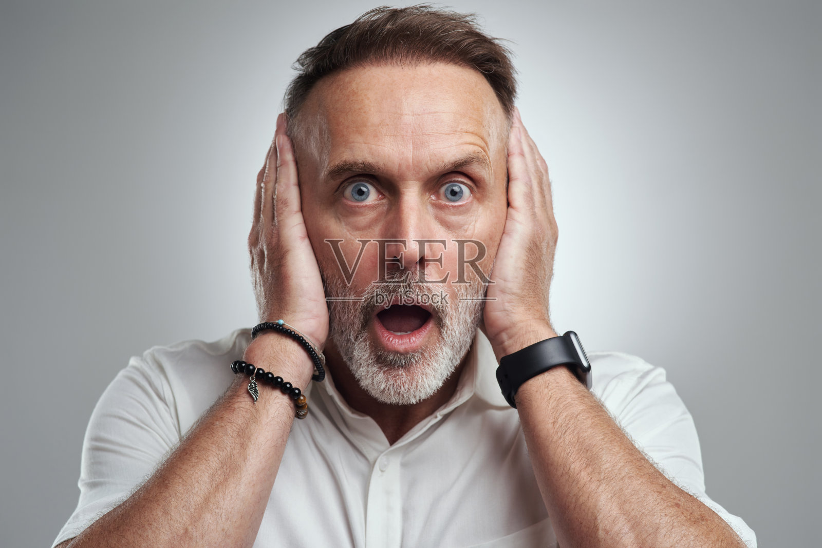 在灰色背景下，一个成年男子捂着耳朵，看起来很震惊照片摄影图片