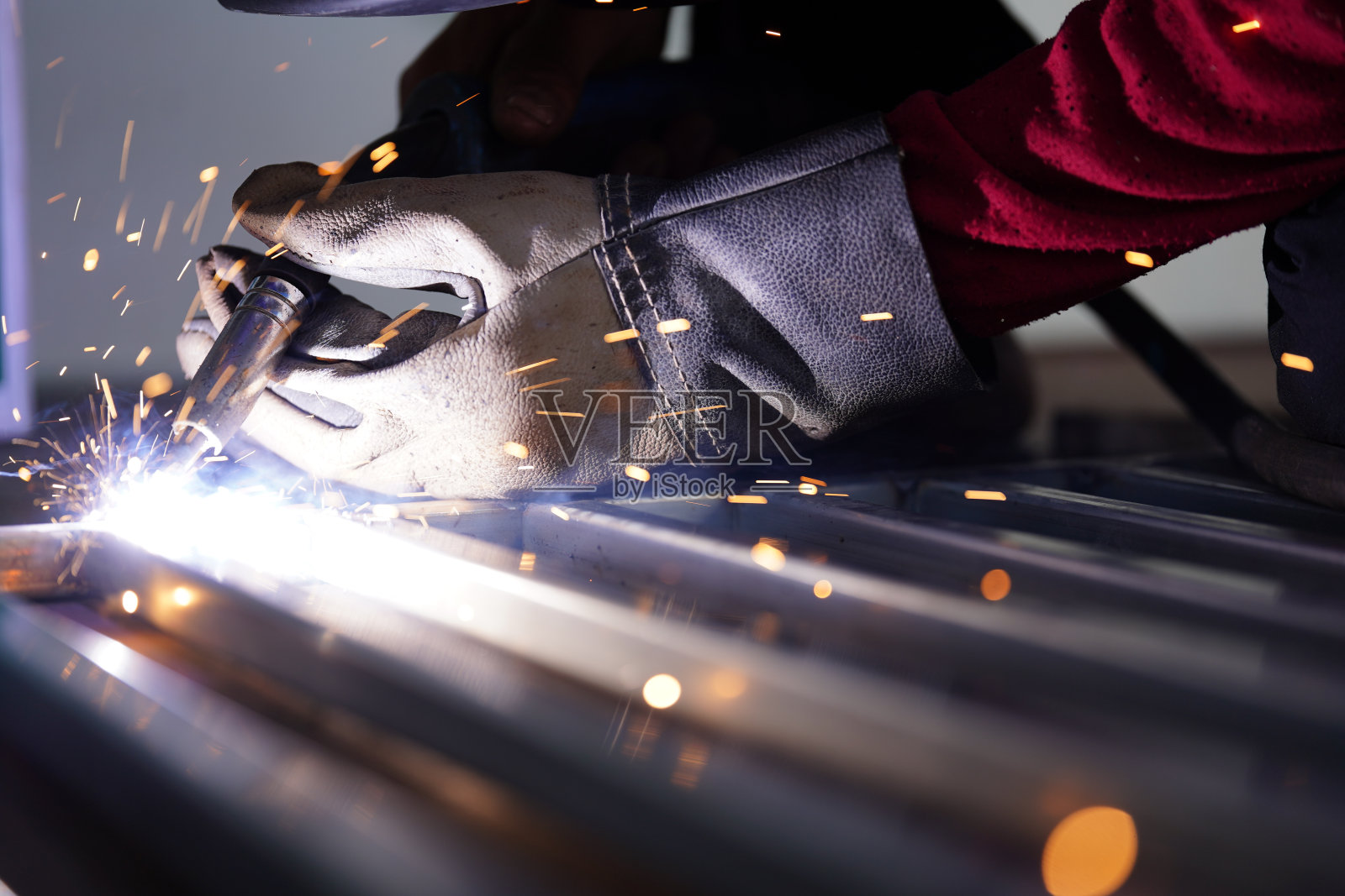 一位戴着手套的亚洲焊接工人正在焊接一根小管子，钢制工件上冒着烟和火花。照片摄影图片