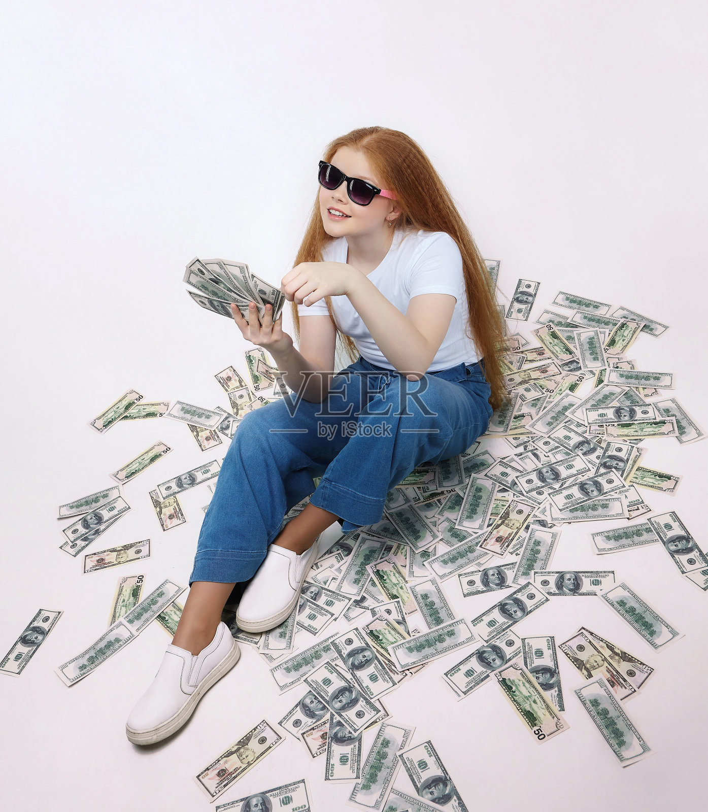 漂亮的红头发女孩坐在钱上。美元散落在地上照片摄影图片