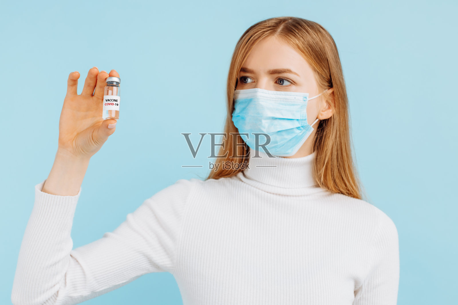 医生拿着一个小瓶，上面有一剂注射用的冠状病毒疫苗，背景为蓝色照片摄影图片