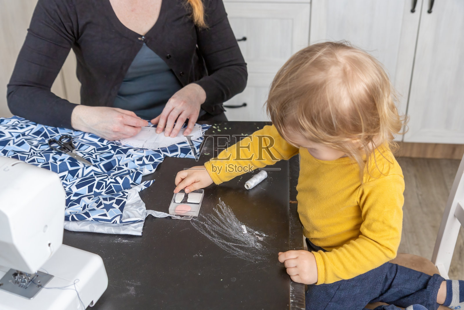 年轻的母亲在做针线活，而她的小儿子在玩粉笔照片摄影图片