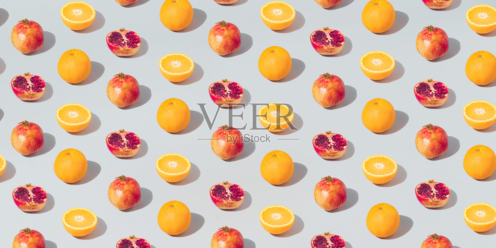 图案用鲜橙、石榴和切成的灰色背景。最少的水果或食物概念。平躺，俯视图。照片摄影图片