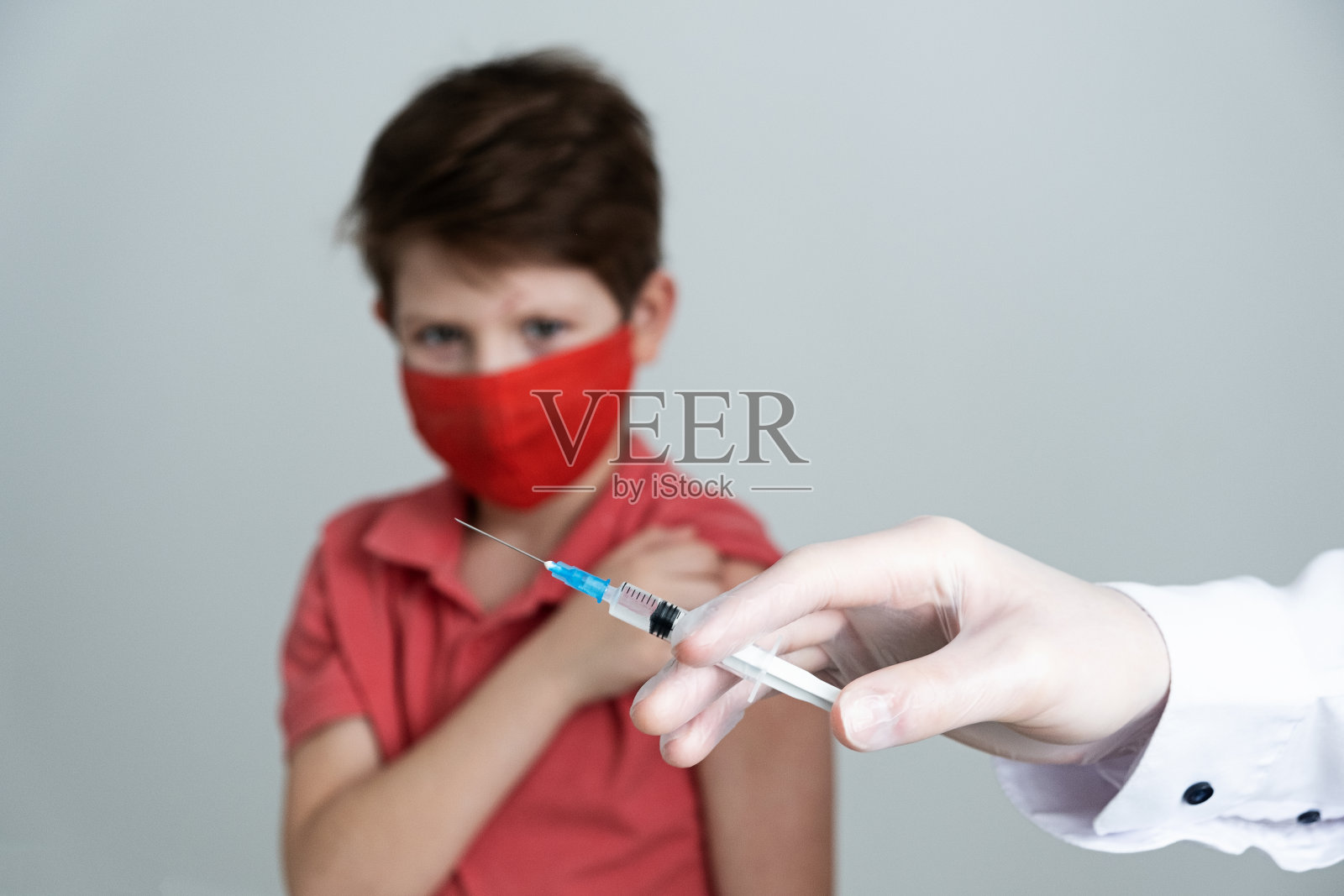 2019冠状病毒病大流行期间，一名戴着医用口罩的儿童接种了抗冠状病毒疫苗。医生在医疗手套与注射器进行注射。本空间照片摄影图片