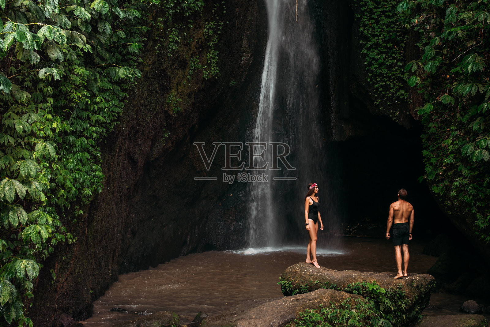 一对夫妇在热带瀑布。这对夫妇前往印度尼西亚的巴厘岛。一个女人和一个男人在美丽的瀑布旁。在热带岛屿上度假。一对在瀑布边旅行的夫妇照片摄影图片