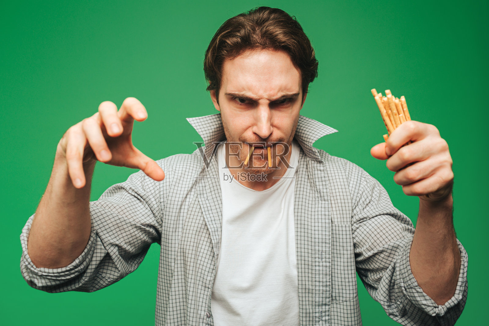 年轻人玩着稻草，假装是德古拉，在绿色背景上被孤立照片摄影图片