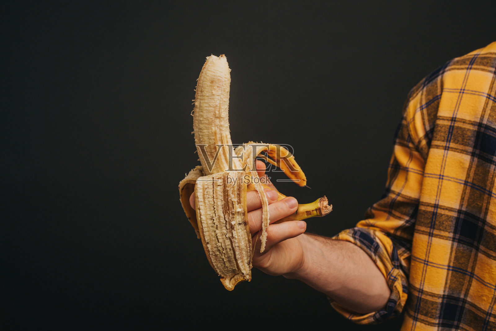 近距离看，穿着黄衬衫的金发男子正拿着香蕉，在黑色的背景下孤立无间照片摄影图片