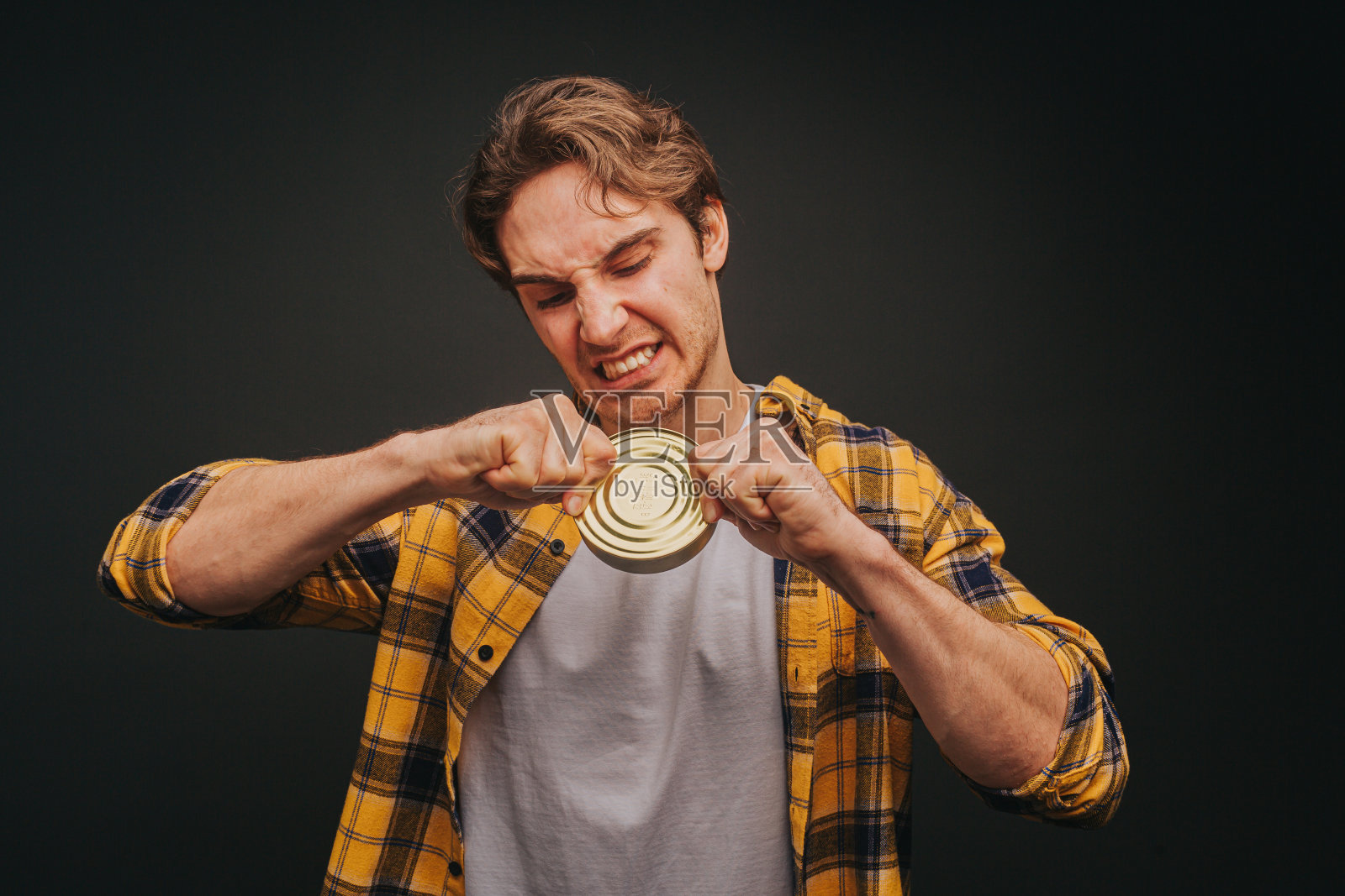 穿着黄色衬衫的金发男子正在打开一个罐头，在黑色的背景下与世隔绝照片摄影图片