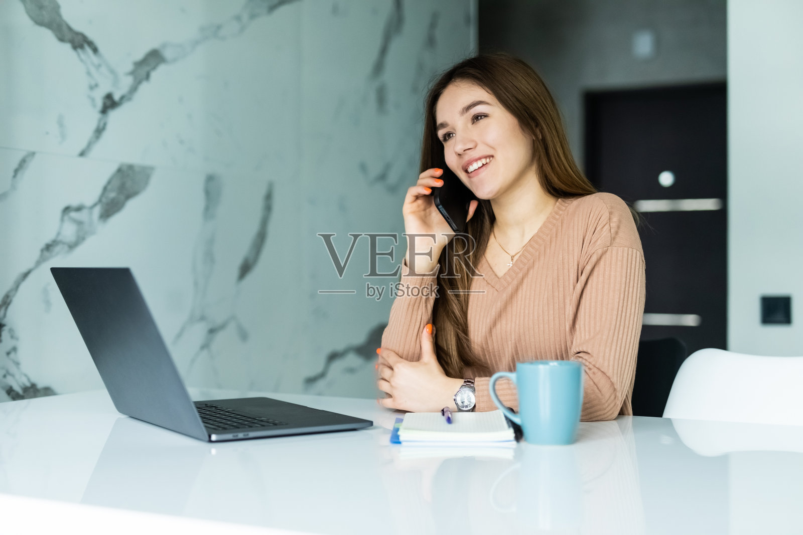 一名年轻女子坐在餐桌旁，用笔记本电脑和手机聊天照片摄影图片
