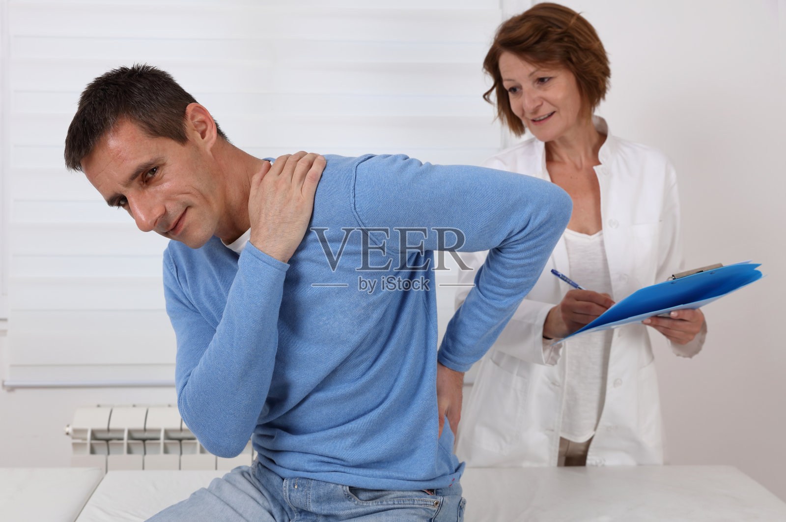 医生和病人在医疗检查期间遭受下腰和颈部疼痛。捏脊、理疗概念。照片摄影图片