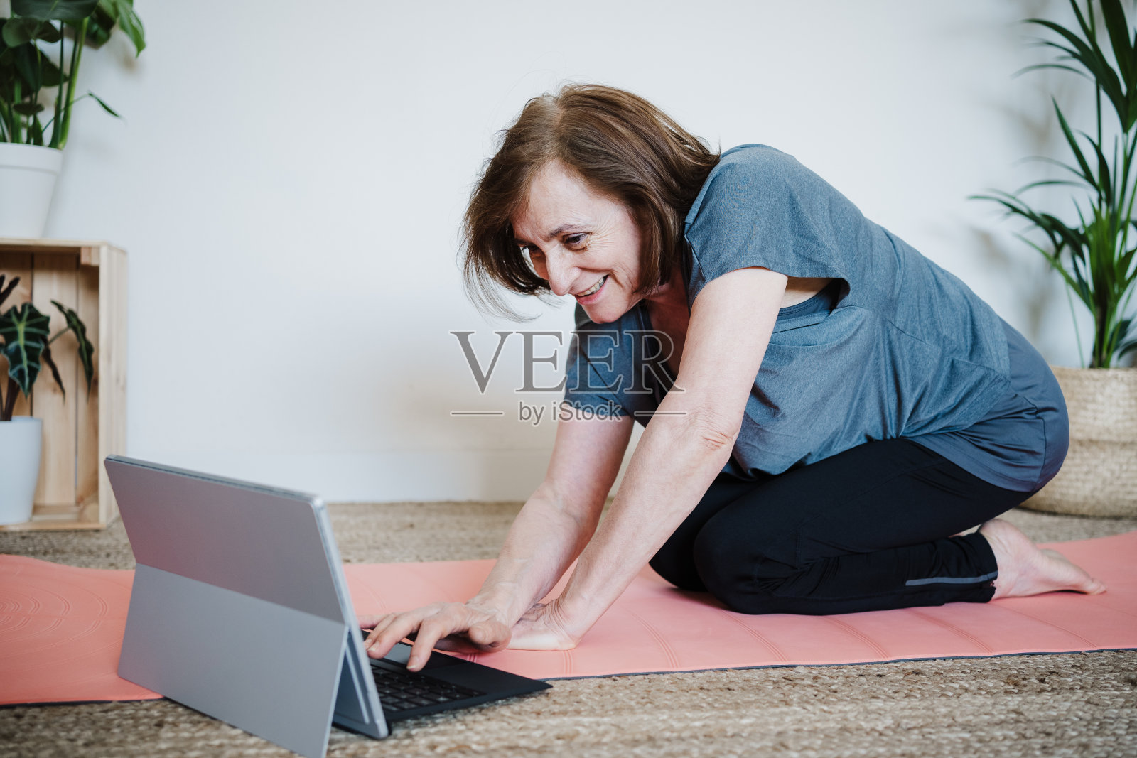 近距离观察成熟的白人年长的妇女在家里练习瑜伽姿势。使用笔记本电脑与老师在线上课。健康的科技生活方式照片摄影图片