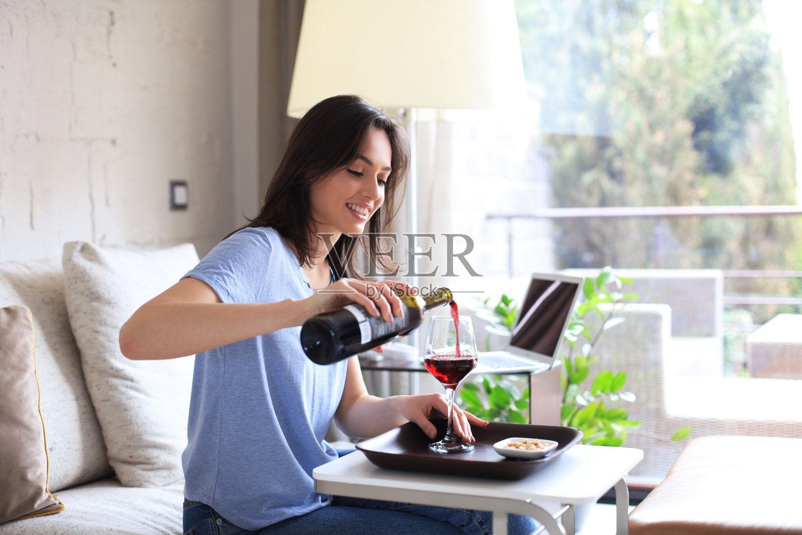 成功的年轻美女坐在客厅的沙发上，喝着红酒。照片摄影图片