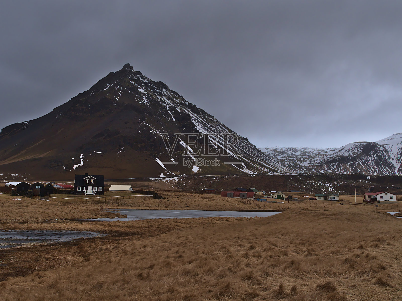 小村庄Arnarstapi, sn æfellsne的一部分，在Snæfellsnes海岸，冰岛多云的冬日，冰冻的湖，棕色的草地和崎岖的雪山。照片摄影图片