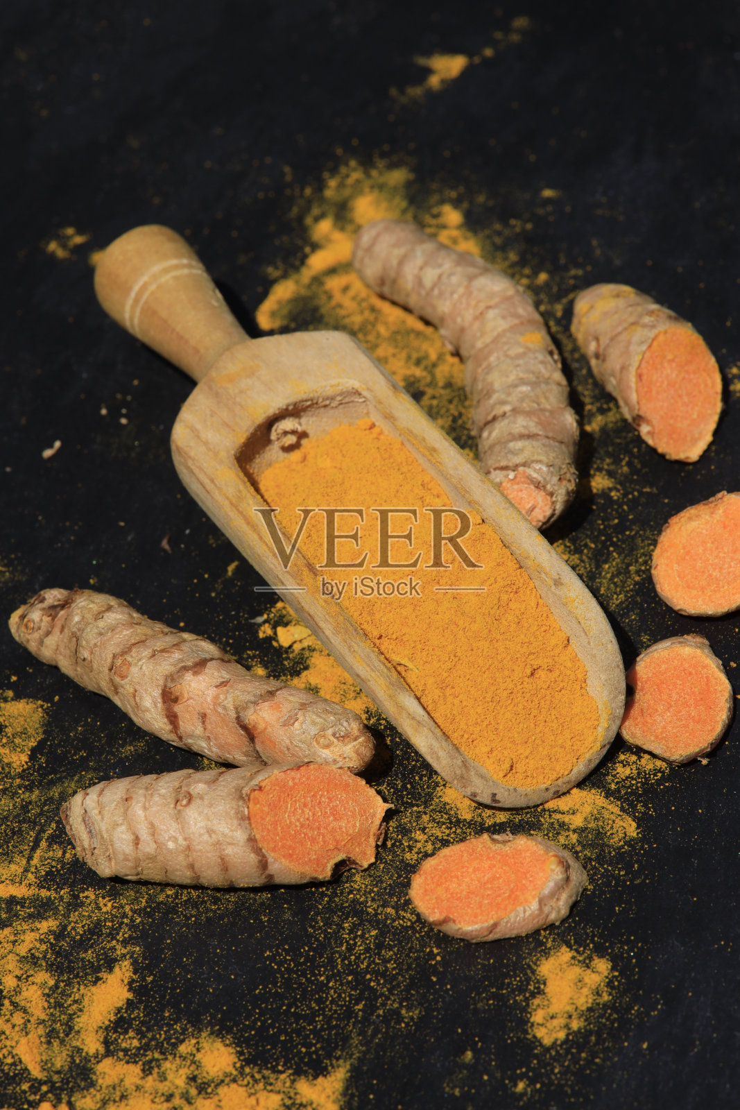 姜黄粉放在木勺里，根放在深色的桌子上(姜黄)，Kurkuma照片摄影图片