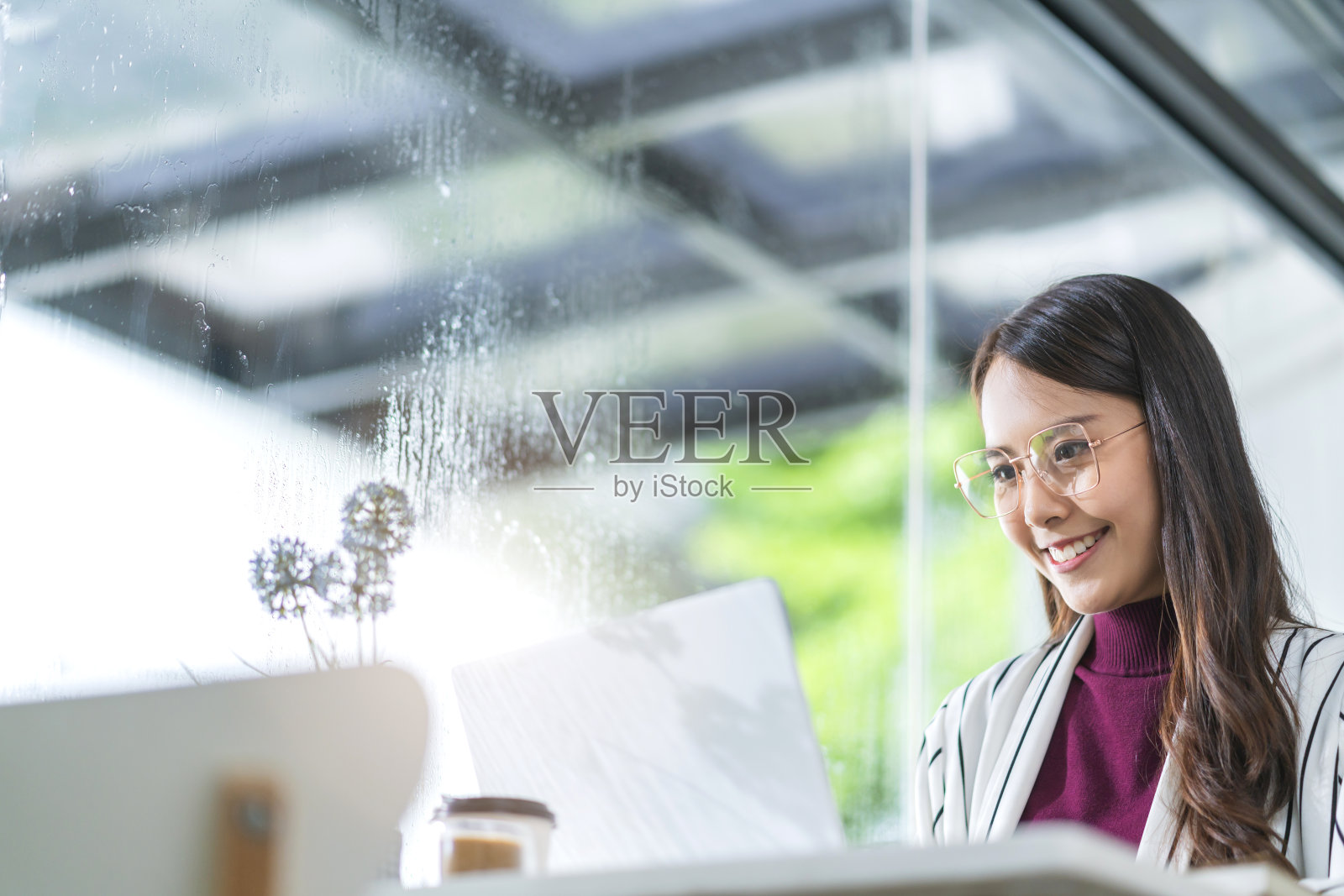 年轻迷人的亚洲女性穿休闲服，手用智能手机和笔记本电脑设备交流，社交，在咖啡馆，餐厅，坐在柜台旁边的大窗户采光照片摄影图片