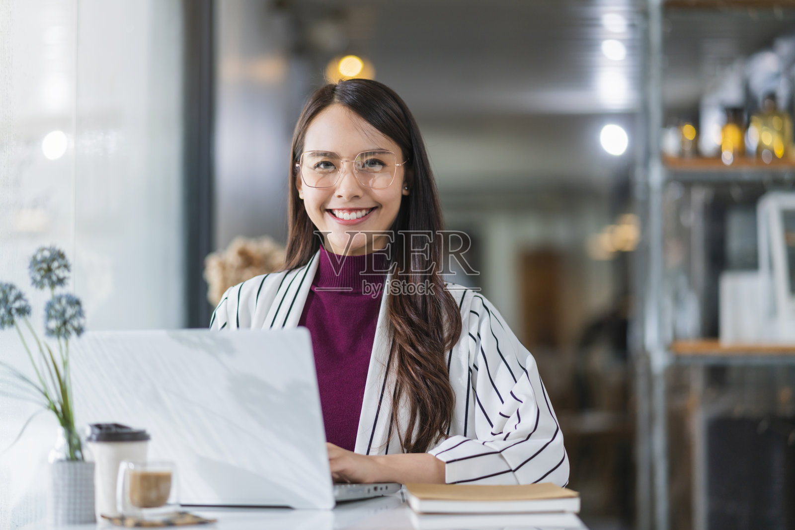 年轻迷人的亚洲女性穿休闲服，手用智能手机和笔记本电脑设备交流，社交，在咖啡馆，餐厅，坐在柜台旁边的大窗户采光照片摄影图片