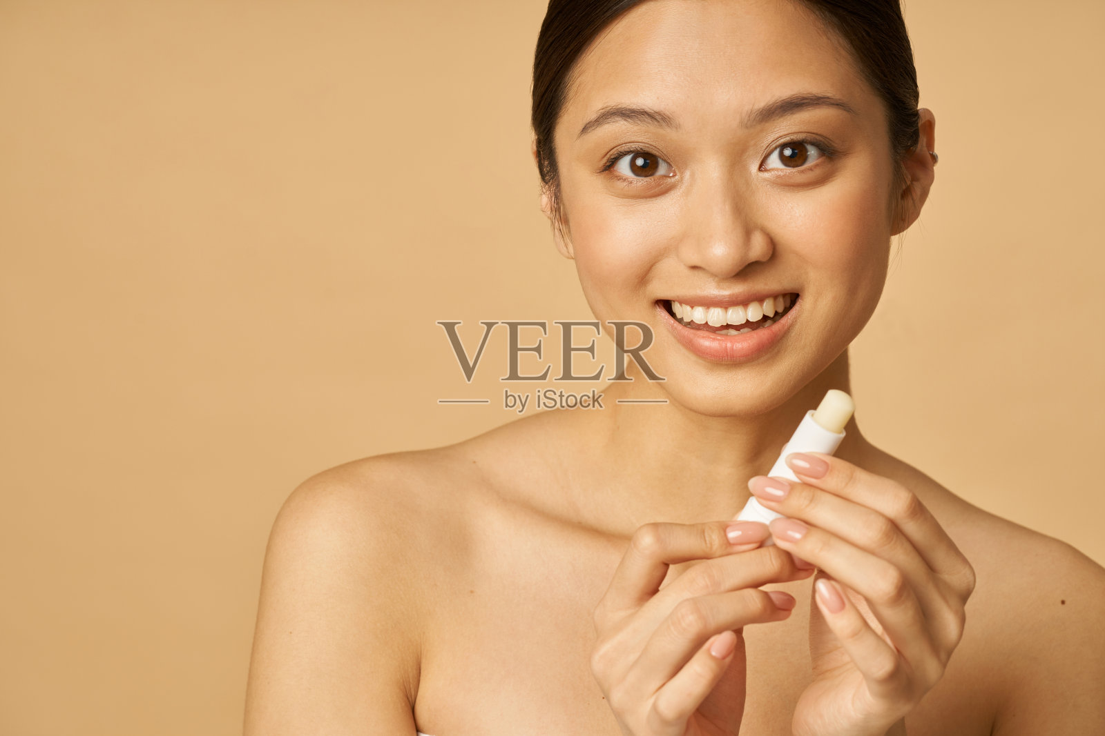 可爱的年轻女子微笑的肖像，而持有唇膏，摆出孤立的米色背景照片摄影图片