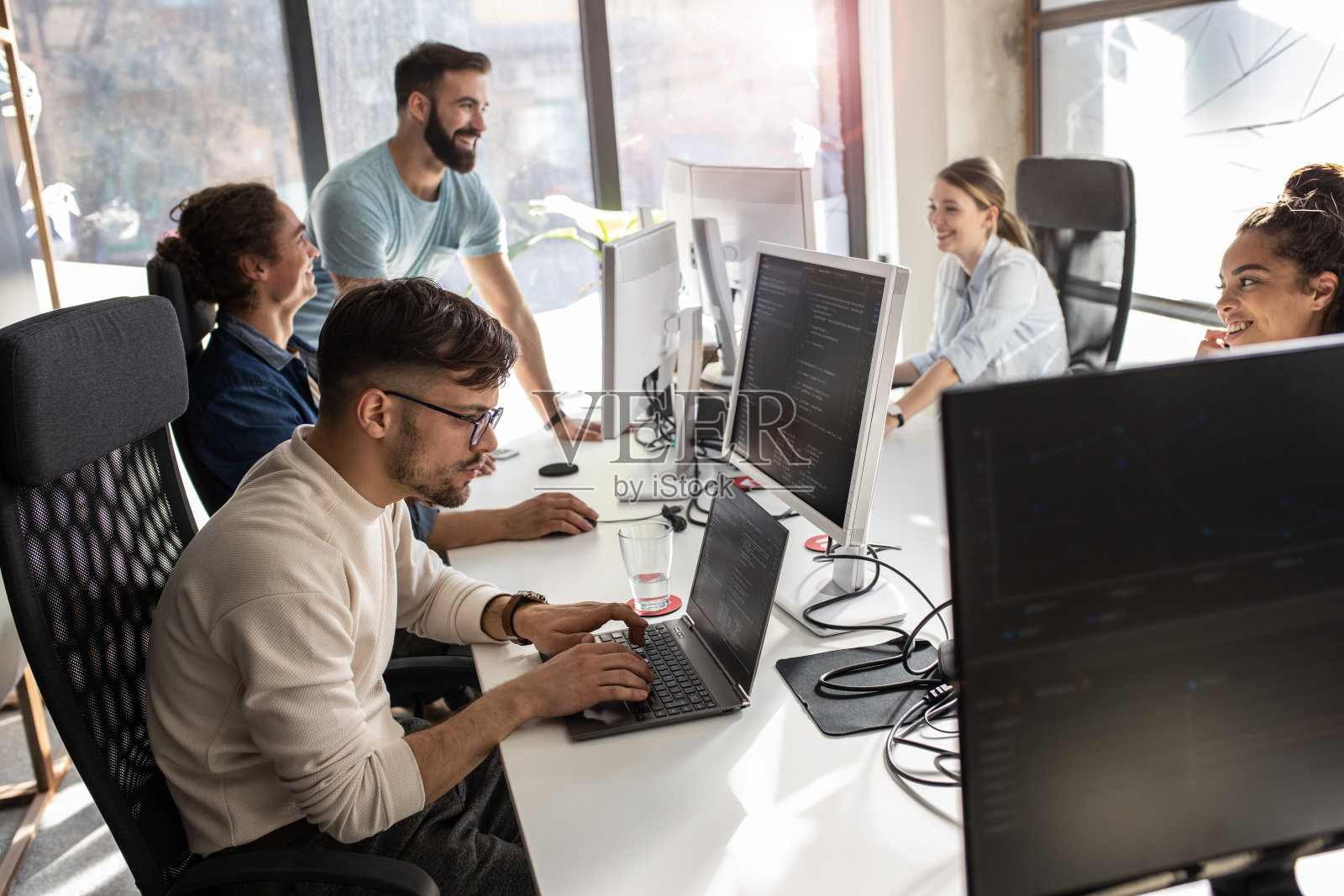 年轻的男性程序员坐在他办公室的办公桌前工作。照片摄影图片