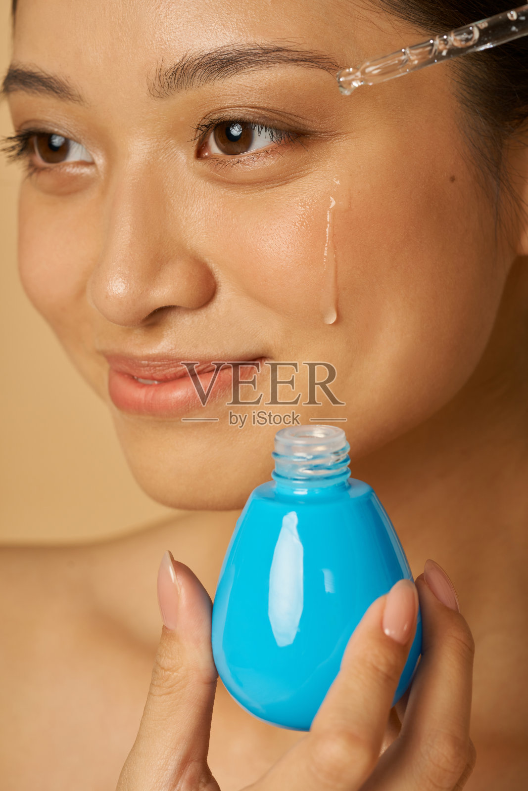 脸部特写美丽的年轻女子滴油血清与移液管在脸上为新鲜完美的皮肤隔离在米色背景照片摄影图片