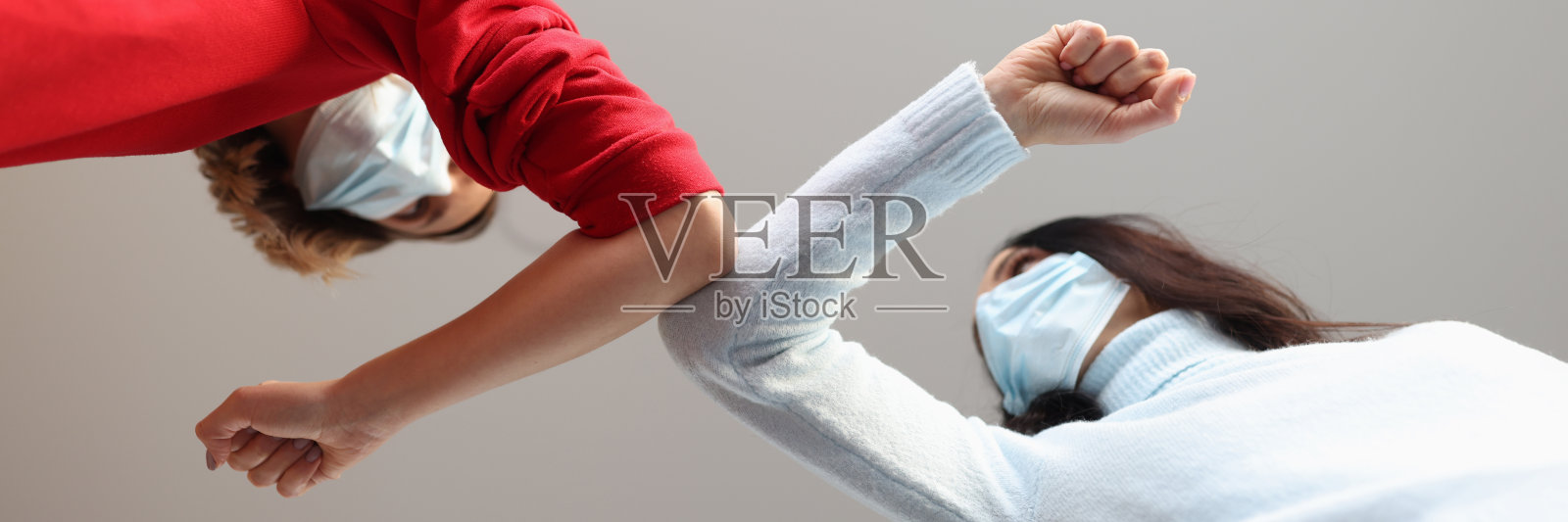 两名戴着医用口罩的妇女用手肘互相触碰照片摄影图片