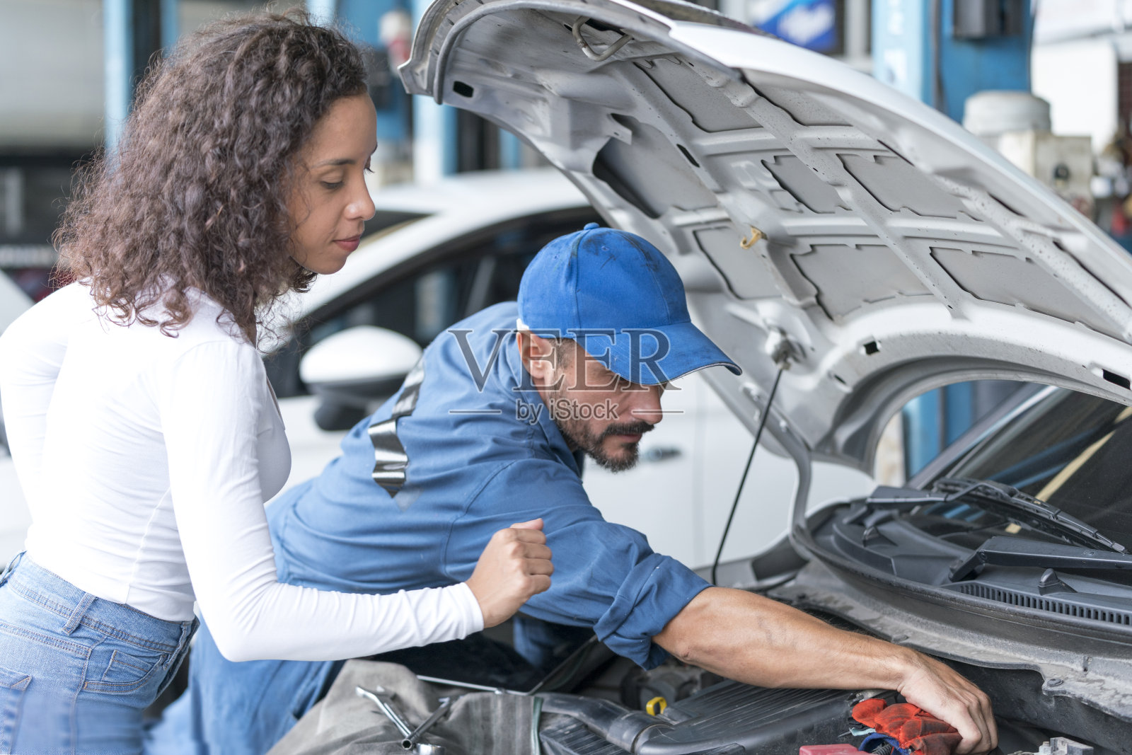 汽车服务和小型企业的概念。在车间修车的技工正在修理汽车。技术人员正在向客户解释汽车的故障。照片摄影图片