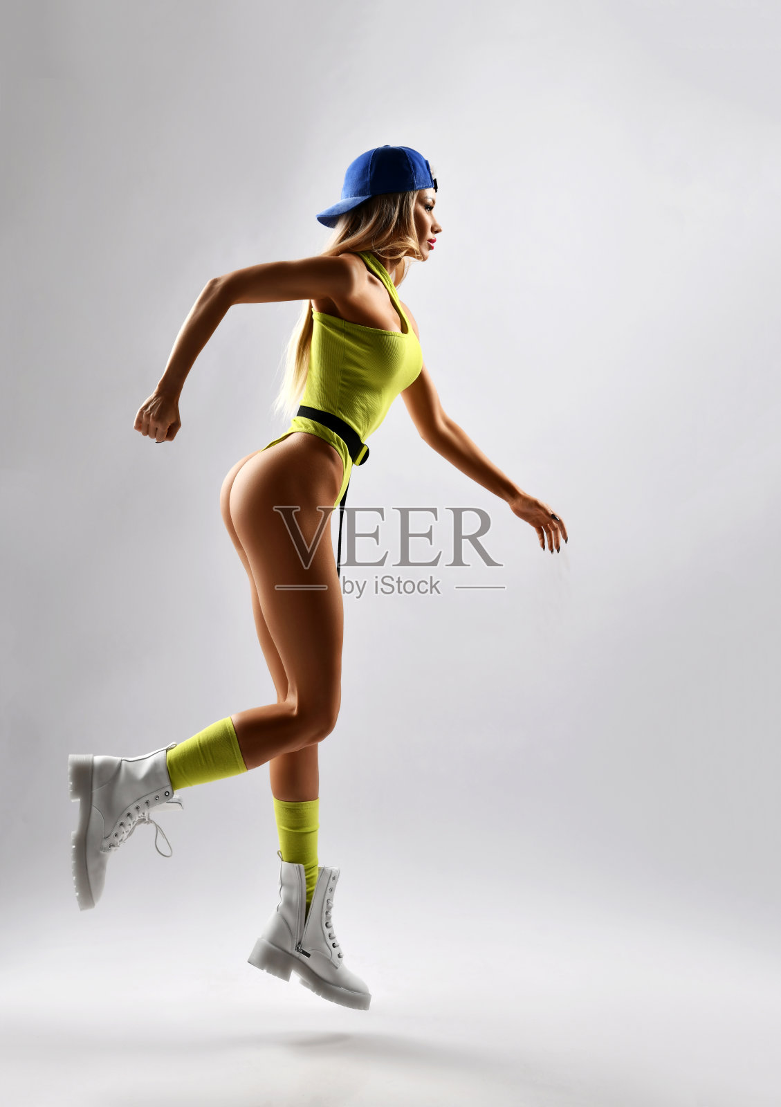 性感的健身教练漂亮的金发女人黄色泳衣，蓝色的帽子和白色的大鞋子跳慢跑照片摄影图片