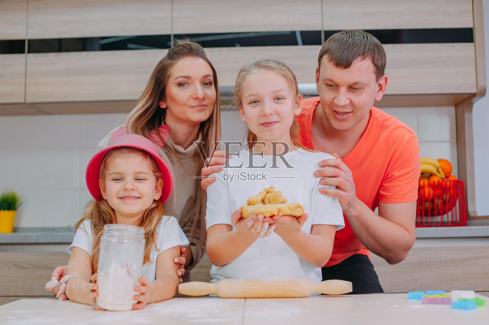 妈妈和爸爸教两个女儿在厨房做面团。照片摄影图片