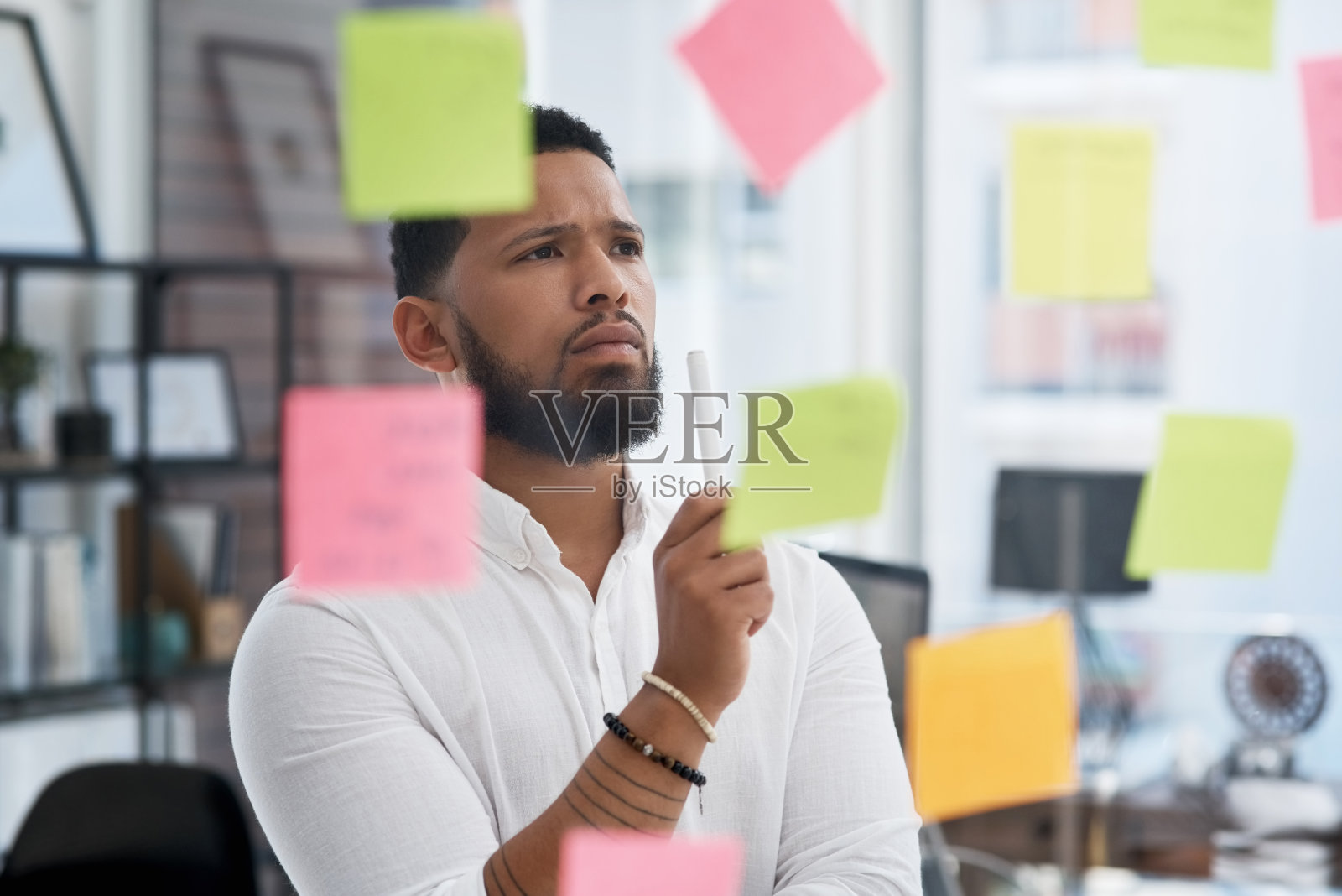 这是一个年轻的商人在办公室的玻璃墙上用便利贴进行头脑风暴的照片照片摄影图片
