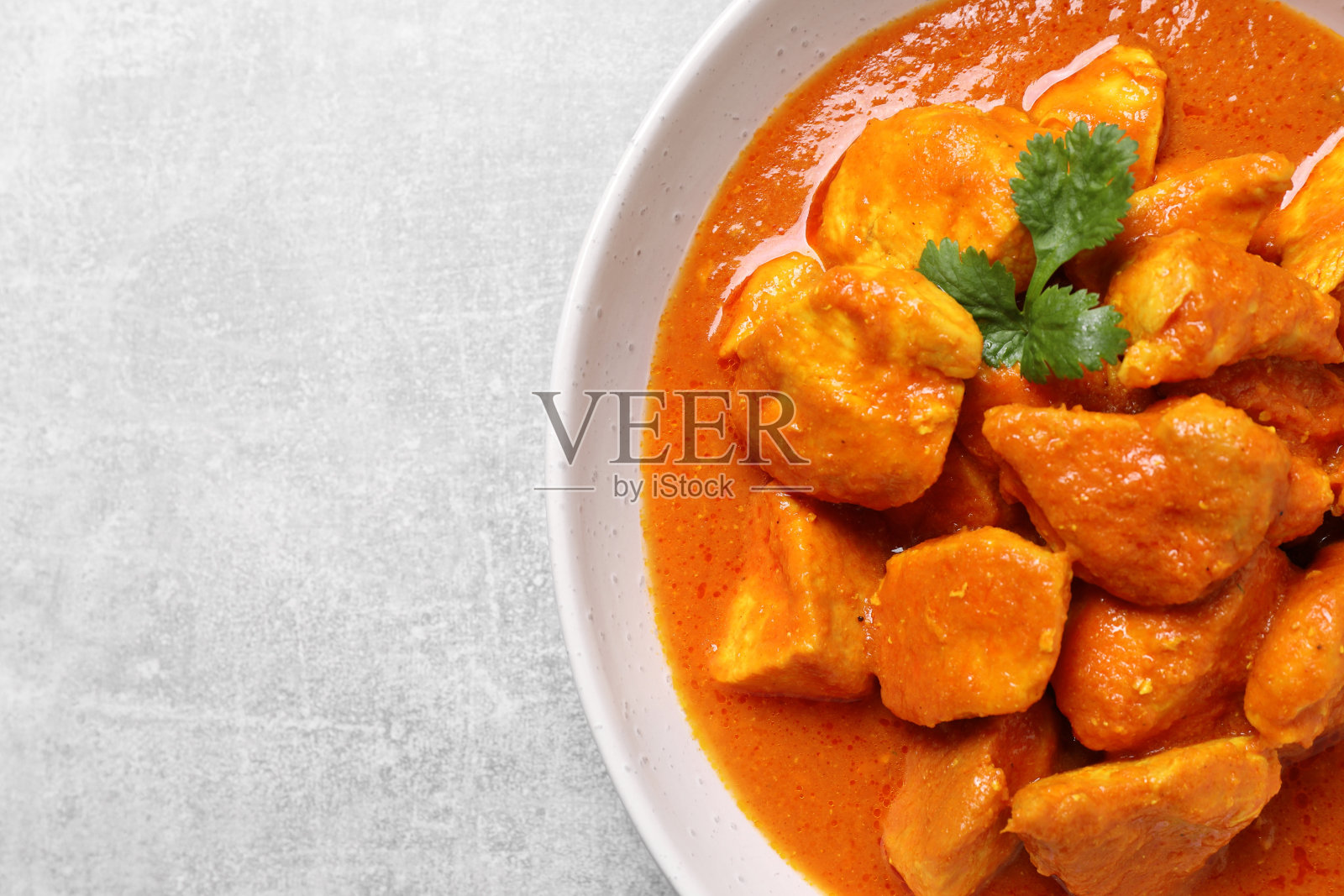 浅灰色的桌子上放着一碗美味的咖喱鸡，俯视图。空间的文本照片摄影图片