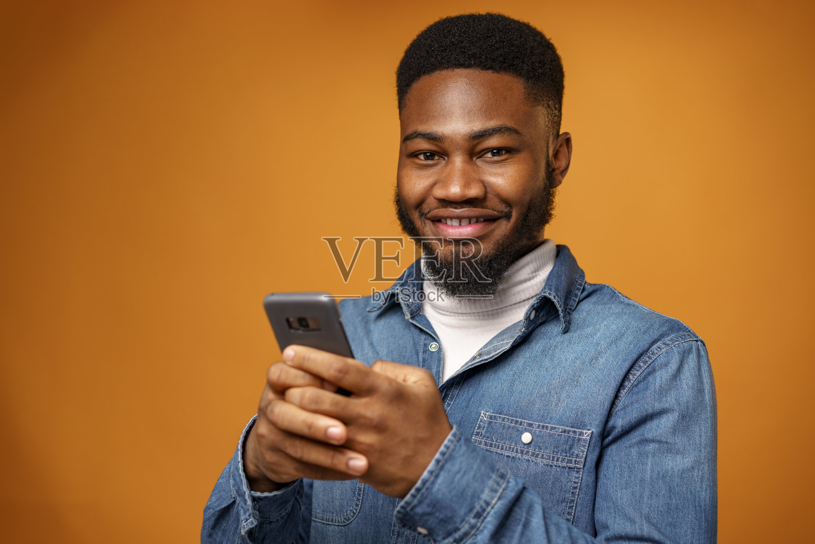 一个年轻的非裔美国人在黄色背景下使用他的智能手机照片摄影图片